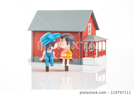 Miniature couple sharing a kiss in front of a charming red house at sunset 129797111