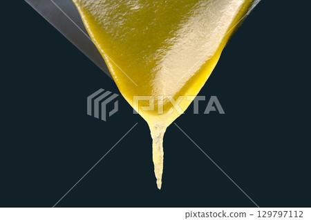 Thick yellow liquid pouring from a metallic surface against a dark backdrop 129797112