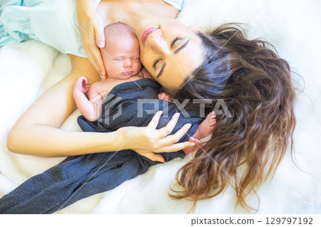 Mother gently cradles her newborn baby in a cozy and serene setting at home 129797192