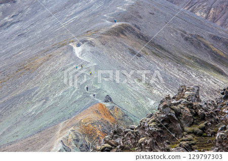 Hikers explore the rugged terrain of Landmannalaugar in Iceland on a bright sunny afternoon 129797303