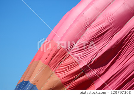 Colorful hot air balloon preparing for flight against clear blue sky Colorful hot air balloon preparing for flight against clear blue sky 129797308