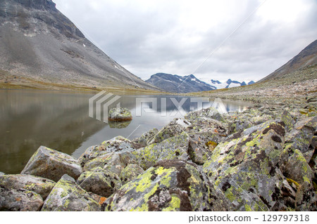 Calm lake reflecting surrounding mountains in Norway's serene landscape during overcast weather Calm lake reflecting surrounding mountains in Norway's serene landscape during overcast weather 129797318