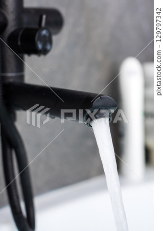 Modern Black Faucet with Flowing Water in a Stylish Bathroom Modern Black Faucet with Flowing Water in a Stylish Bathroom 129797342