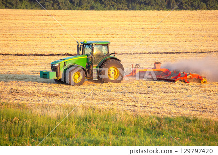 Tractor plowing golden field at sunset in rural farmland 129797420