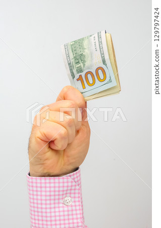 Hand holding a hundred dollar bill in the air against a plain backdrop 129797424