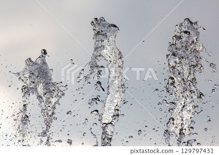 Fountain water splashes create stunning patterns under gray sky during a sunny day 129797431
