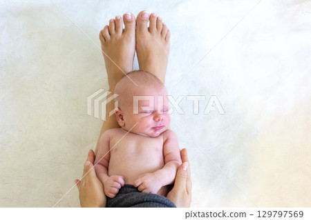 Newborn baby resting peacefully on a parent's legs in a cozy indoor setting 129797569