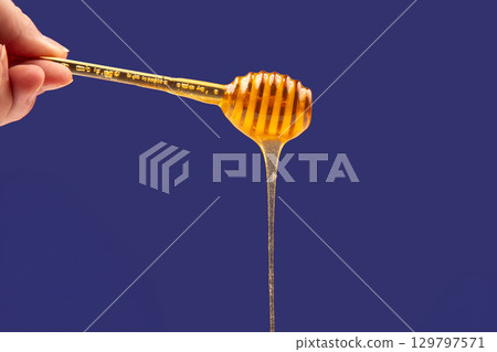 Honey drips from a wooden dipper against a vibrant blue background 129797571