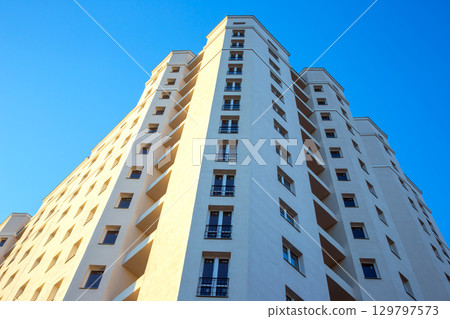 Modern apartment building reaching towards a clear blue sky in a vibrant urban setting 129797573