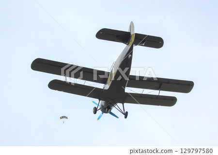 Skydiver descending from a biplane against a clear blue sky at an outdoor event 129797580
