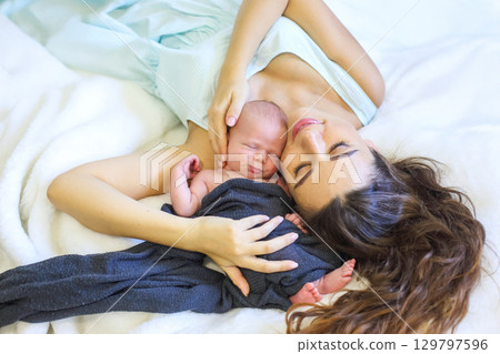 New mother lovingly holds her newborn baby on a cozy blanket in a warm setting 129797596
