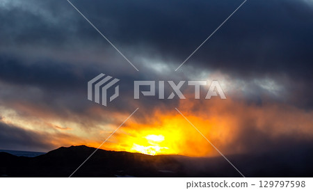 Sunset over Icelandic landscape with clouds and warm hues illuminating the horizon 129797598