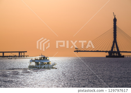 Boat on Tamsui River with Bridge Construction at Sunset, New Taipei City. 129797617