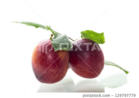 Ripe red plums and green leaves on a white background 129797779