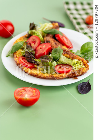 Delicious omelette on a plate with fresh leaves and tomato slices 129797804