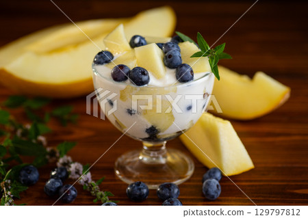 Glass bowl of yogurt with melon pieces and blueberries on a wooden Glass bowl of yogurt with melon pieces and blueberries on a wooden 129797812
