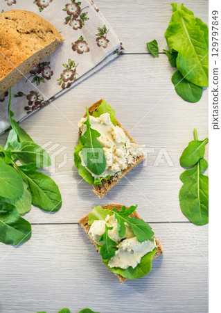 Close-up of a sandwich with herring and salad leaves on a light wooden table 129797849