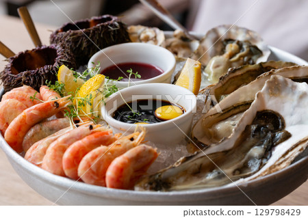 Seafood (oysters, shrimps, sea-urchins, mussels) are decoratively put on ice in a big plate Seafood (oysters, shrimps, sea-urchins, mussels) are decoratively put on ice in a big plate 129798429