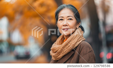 Mature Asian woman standing seriously on a street in autumn. Mature Asian woman standing seriously on a street in autumn. 129798586