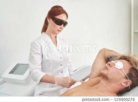 Female caucasian adult performing laser hair removal on male young adult 129800278