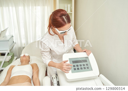 Female technician operating laser device for skin treatment with relaxed patient Female technician operating laser device for skin treatment with relaxed patient 129800314