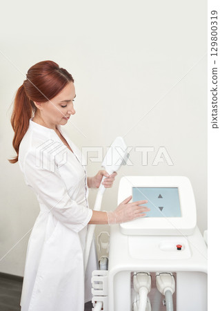 Caucasian female technician operates laser hair removal machine in clinic 129800319