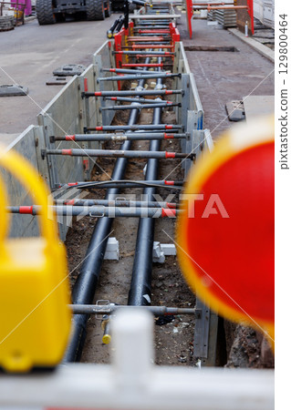 Urban street excavation with visible pipelines and safety barriers. Red warning lights and construction fencing mark the site in a residential area under infrastructure repair 129800464