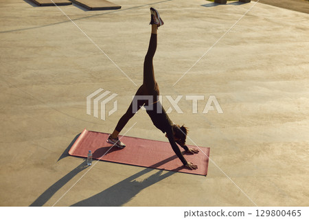 Sporty athletic woman exercising on yoga mat outdoors. Fitness and workout concept. 129800465
