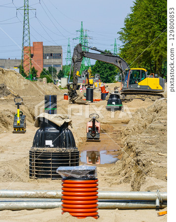 Excavator and utility installation at construction site with pipes, manholes, and power lines Excavator and utility installation at construction site with pipes, manholes, and power lines 129800853
