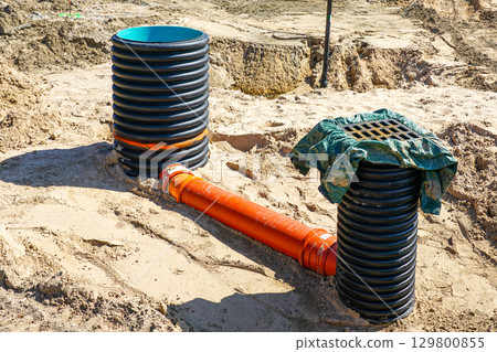 Sewer and rainwater manholes with connecting drainage pipe on sandy construction site 129800855