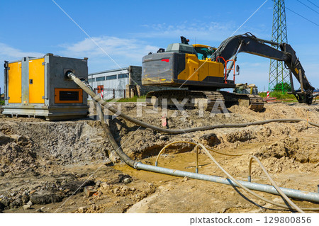 Construction site with dewatering pump, pipes, and excavator during groundwater removal process Construction site with dewatering pump, pipes, and excavator during groundwater removal process 129800856