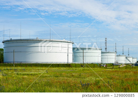 Large industrial oil storage tanks in field with blue sky at petroleum facility 129800885