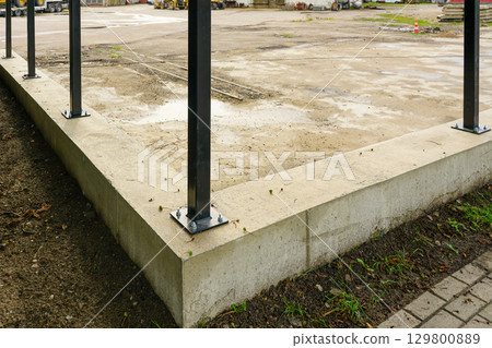 New fence construction with concrete foundation and anchored black metal posts at worksite 129800889