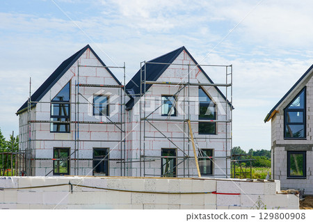 Modern two-story house under construction with scaffolding and unfinished exterior walls 129800908
