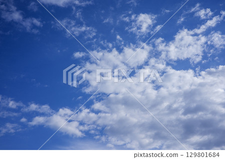 A photorealistic image of a blue sky with white clouds, showcasing a vast expanse of clear blue sky with scattered white clouds of various shapes and sizes. The clouds are fluffy and appear to be 129801684