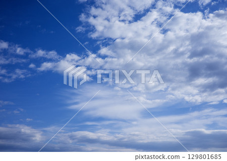 A photorealistic image of a blue sky with white clouds, showcasing a vast expanse of clear blue sky with scattered white clouds of various shapes and sizes. The clouds are fluffy and appear to be 129801685