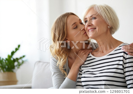 Young woman kissing her elderly mother on the cheek at home 129801701
