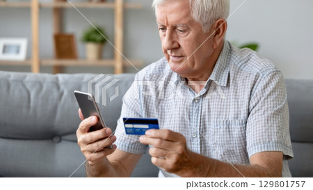 Focused senior man using smartphone and credit card for online shopping at home Focused senior man using smartphone and credit card for online shopping at home 129801757