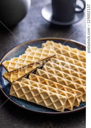 Sweet crispy wafers on plate on black table. 129802137