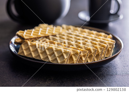 Sweet crispy wafers on plate on black table. 129802138