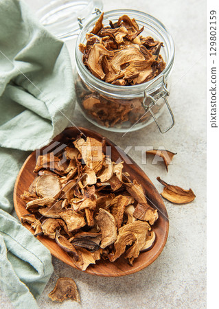 Dried mushrooms on wooden plate with fresh mushrooms and jar 129802159