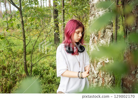 Young relaxed girl listening music leaning against birch in forest 129802170