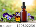 Essential oil bottle with dropper surrounded by pansies on wooden table 129802230