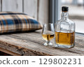 Glass and bottle of whisky resting on rustic wooden table 129802231