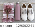 Cozy pink blanket, metal water bottle, and white sneakers on rustic wood background 129802241