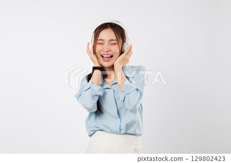 Music flows as happy woman closes eyes and smiles while listening through headphones, enjoying lifestyle peace and connection with calming music. isolated studio white background 129802423