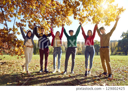 Group of happy young friends having fun under beautiful trees in sunny autumn park Group of happy young friends having fun under beautiful trees in sunny autumn park 129802425