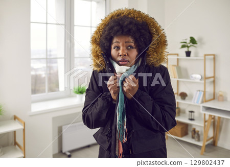 Unhappy young woman feeling cold wearing warm winter jacket indoors Unhappy young woman feeling cold wearing warm winter jacket indoors 129802437