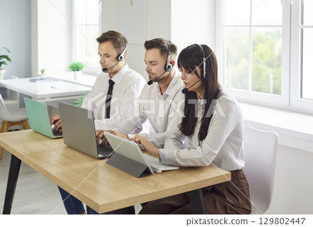Helpdesk team with headsets at laptops in office, providing customer support 129802447