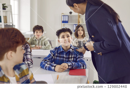 Woman teacher in junior high school helping a boy during a lesson in the classroom. 129802448